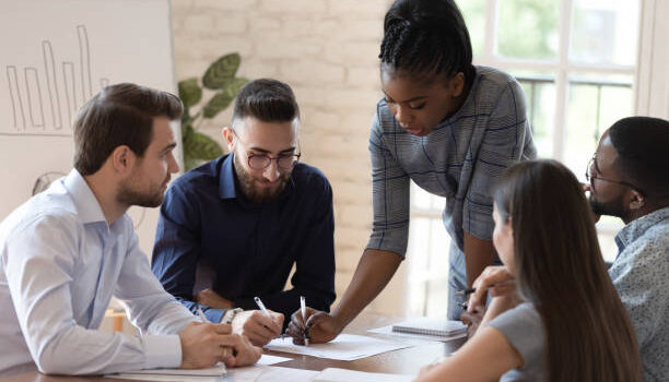 Serious african woman supervisor boss teach diverse staff workers explain project plan paperwork at group meeting, focused black female mentor training business team at corporate office briefing